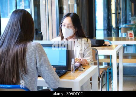 Zwei Schülerinnen mit Gesichtsmasken, die in einem Restaurant an ihren Computern arbeiten. Neue Normalität in Restaurants. Coronavirus-Pandemie. Stockfoto