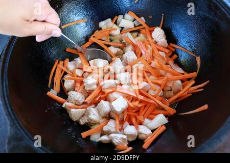 Person mischt Fleisch mit Zwiebeln und Karotten in Kessel für Pilaf Stockfoto