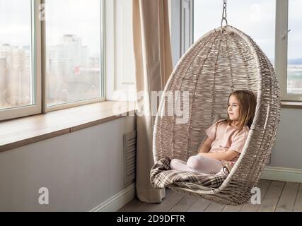 Nettes Mädchen sitzt in einem hängenden Stuhl und schaut aus Das Fenster Stockfoto