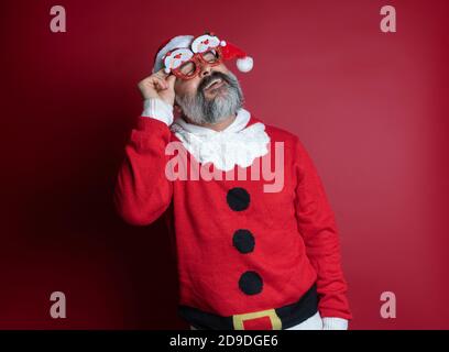 Mann im Weihnachtspullover mit roten Hintergrund Party Brille Stockfoto