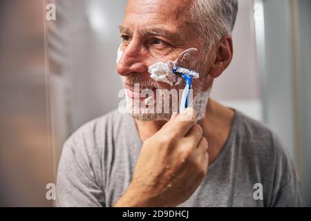 Fröhlicher alter Mann mit einem Rasiermesser, der eine Rasur vorgeht Stockfoto