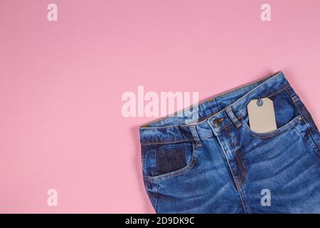 Unbeschriftete Label Preisschild-Label mit blauer Jeans auf hellrosa Hintergrund. Draufsicht Stockfoto