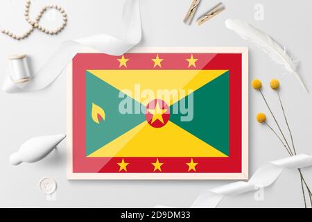 Grenada Flagge in Holzrahmen auf weißem kreativen Hintergrund. Weißes Thema, Feder, Gänseblümchen, Knopf, Band-Objekte. Stockfoto