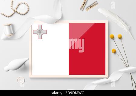 Malta Flagge in Holzrahmen auf weißem kreativen Hintergrund. Weißes Thema, Feder, Gänseblümchen, Knopf, Band-Objekte. Stockfoto