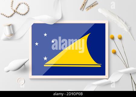 Tokelau Flagge in Holzrahmen auf weißem kreativen Hintergrund. Weißes Thema, Feder, Gänseblümchen, Knopf, Band-Objekte. Stockfoto