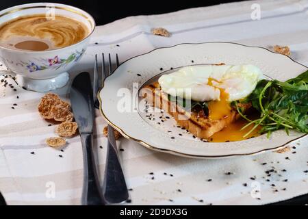 Gesundes Frühstück mit pochiertem Ei auf Toast mit grünen Salatblättern. Und Tasse Kaffee Eigelb Aufstrich Stockfoto