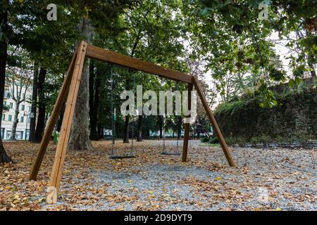 Leere Schaukel für Kinder in einem Park mit heruntergefallenen Blättern. Herbststimmung Stockfoto