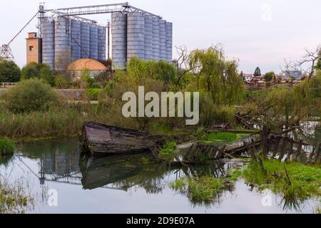 Historischer Friedhof von versunkenen hölzernen Schiffswracks im Wasser in Der Sile Fluss genannt Burci Friedhof mit einer verlassenen Fabrik Mit Silos im Hintergrund Stockfoto