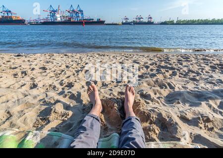 Entspannung am Strand an der Elbe in Hamburg Mit Hafenanlagen und Containerschiffen im Hintergrund Stockfoto