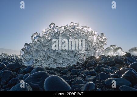 Schmelzende Eisbergfragmente auf dem schwarzen Basalt-Kiesstrand Von Jokulsarlon Island - Sonne schmelzendes Eis - globale Erwärmung - Klimawandel Stockfoto