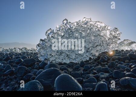 Schmelzende Eisbergfragmente auf dem schwarzen Basalt-Kiesstrand Von Jokulsarlon Island - Sonne schmelzendes Eis - globale Erwärmung - Klimawandel Stockfoto