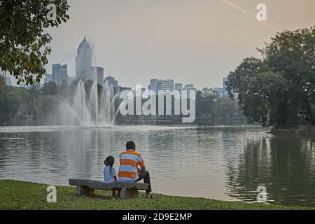 Bangkok, Thailand, März 2106. Ein Vater und seine Tochter sitzen auf einer Bank und blicken über den See im Lumpini Park. Stockfoto