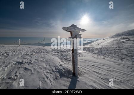 Schneebedeckter Zeiger in der Nähe von Pfad auf verschneiten Bergplateau und Sonnenschein am Himmel. Herrlicher sonniger Tag auf malerisch schönem alpenrücken. Stockfoto