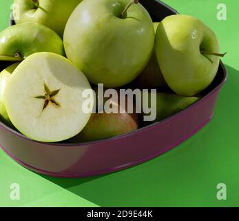 Grüne Äpfel, ganz und Hälften in Metallform auf grünem Hintergrund. Frische Ernte zum Entsaften, Smoothie-Pasteten und gesunde Lebensmittel. Stockfoto