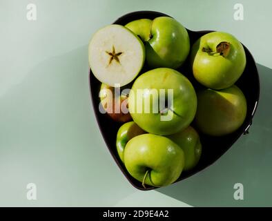 Grüne Äpfel ganz und herzförmige Hälften. Die Backform ist mit frischen Äpfeln gefüllt. Stockfoto