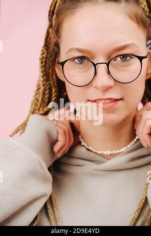 Porträt einer attraktiven Frau in einer Brille mit blondem Afro Zöpfe über Rosa Stockfoto