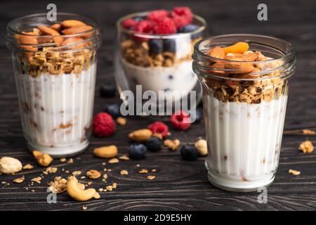 Köstliches Müsli mit getrockneten Aprikosen, Nüssen und Joghurt in Glasbechern auf Holzoberfläche auf verschwommenem Hintergrund Stockfoto