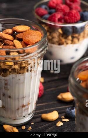 Nahaufnahme von köstlichem Müsli mit getrockneten Aprikosen, Nüssen und Joghurt in Glasbecher auf verschwommenem Hintergrund Stockfoto