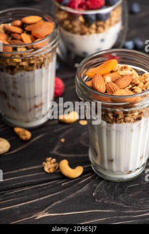 Köstliches Müsli mit getrockneten Aprikosen, Nüssen und Joghurt in Glasbecher auf verschwommenem Hintergrund Stockfoto