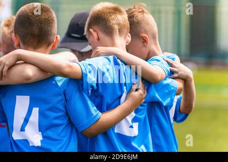 Kinder Fußballmannschaft mit Trainer in der Gruppe huddle vor dem Spiel. Kinder im Grundschulalter hören gemeinsam zu, um motivierende Reden zu coachen. Jungen in blu Stockfoto