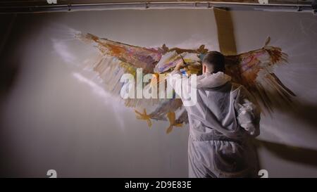 Künstler Designer zieht ein Adler an der Wand. Handwerker Dekorateur malt mit Acryl öl Farbe. Maler Maler gekleidet in Lack auftragen. Indoor. Stockfoto