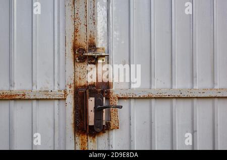 Eiserner rostiger Zaun mit einem Schloss. Weiße Wellblech oder Zink Textur Oberfläche oder galvanisieren Stahl in der vertikalen Linie Hintergrund Stockfoto