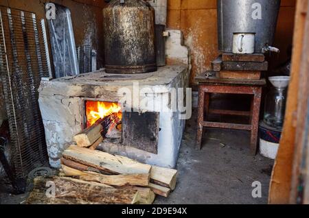 Alte Metall offene Ofentür mit brennendem Holz Flamme. Alte Küche mit großem Topf auf offenem Feuer. Traditionelle Küche auf Holzfeuer Stockfoto