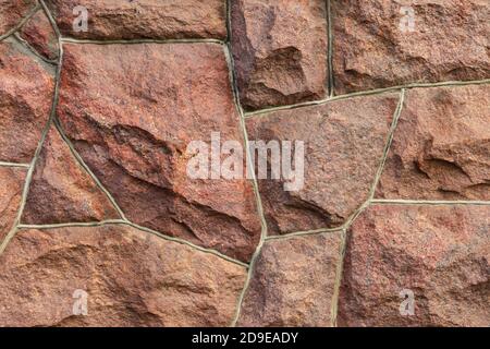 Die Oberfläche des Mauerwerks besteht aus grob behauenen großen roten Steinen, die miteinander verbunden sind. Stockfoto