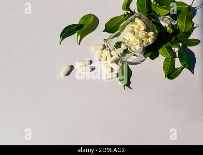 Die Kapseln werden aus einem Glas ausgegossen. Grüne Blätter liegen in der Nähe. Gesundheit und Schönheit Thema. Stockfoto