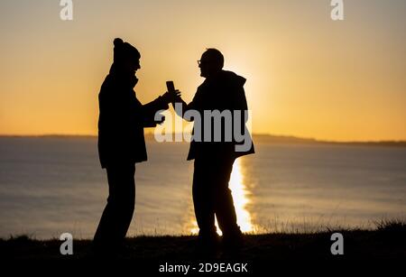 Weymouth, Großbritannien. November 2020. Einheimische machen das Beste aus einem herrlichen Sonnenuntergang zu sehen, die Kreuzfahrtschiffe vor Anker in Weymouth Bay in Dorset mit Freunden am Vorabend der zweiten nationalen Sperre aufgrund der Coronavirus-Pandemie. Quelle: Richard Crease/Alamy Live News Stockfoto