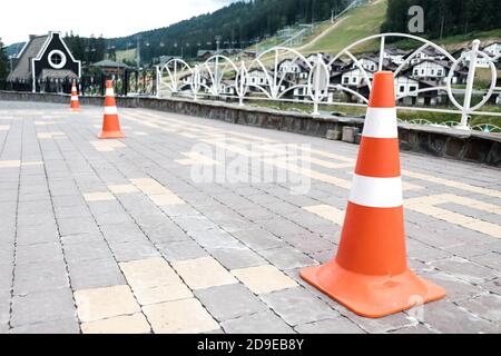 Orange gestreifte Straßenkegel auf einem Bürgersteig. Sicherheitsausrüstung für den Verkehr auf einer Straße, Auto Barrikade Ausrüstung für Fahrunterricht. Sicherheitskonus aus Kunststoff Stockfoto