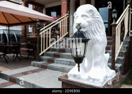 Weiße Löwenstatue mit einer alten Laterne vor einer Hotel- oder Restaurantfassade. Treppe im Hintergrund. Hospitality-Konzept. Sightseeing im Osten Stockfoto