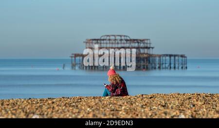 Brighton UK 5. November 2020 - EINE junge Frau sitzt am Brighton Strand an einem schönen sonnigen Tag am ersten Tag der neuen Coronavirus Sperrungen in England, da mehr sonniges Wetter für die nächsten Tage im Süden prognostiziert wird : Kredit Simon Dack / Alamy Live Nachrichten Stockfoto