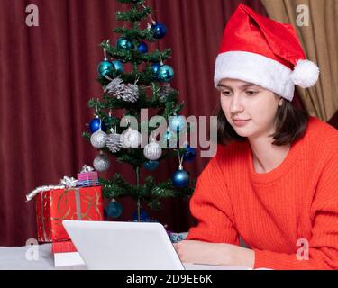 Weihnachtsgrüße im Internet, Bildung, Online-Shopping. Mädchen in einem Weihnachtsmann Mütze mit einem Laptop zu Hause Stockfoto