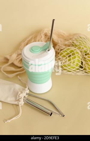Trinkhalm aus Silikon mit Trinkhalmen aus Edelstahl auf beigem Hintergrund mit Netzbeutel. Stockfoto