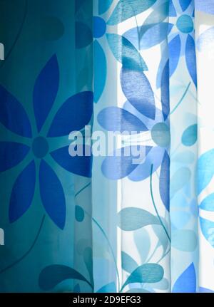 Hintergrund. Ein transparenter Vorhang auf einem blauen Fenster mit blauen Blumen. Licht durch den Vorhang. Stockfoto