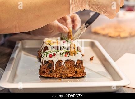 Frauenhände schmücken Weihnachtsfrucht Kuchen mit Lebkuchen, Rosmarin und Preiselbeere. Stockfoto
