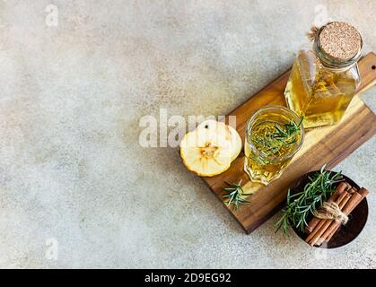 Apfel- oder Birnenmost im hohen Glas und Flasche mit Rosmarin, Zimt und getrockneten Fruchtstückchen, heller Betonhintergrund. Draufsicht. Stockfoto