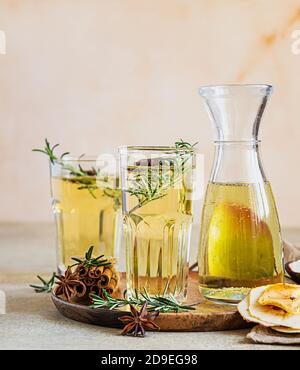 Birne oder Apfelwein in Gläsern und Flasche mit Rosmarin, Zimt und frischen Bio-Birnen. Fermentierter Fruchtdrink. Heller Betonhintergrund. Stockfoto