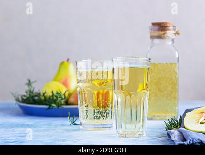 Birnenmost-Cocktail mit Rosmarin in hohen Gläsern und Flasche und frischen Birnen, Hintergrund aus blauem Stein. Erfrischungsgetränk im Sommer. Stockfoto