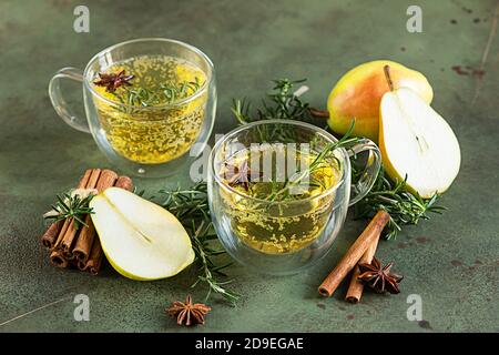 Würzig heiße Birne oder Apfelmost mit Zimt, Anis und Rosmarin. Traditionelle Getränke im Herbst oder Winter. Grüner Betonhintergrund. Stockfoto