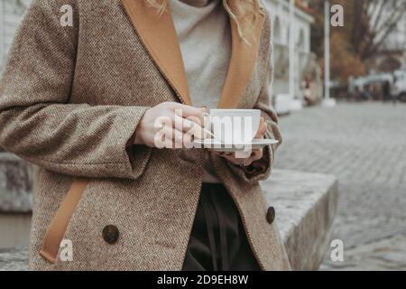 Gesichtsloses Bild einer jungen, stilvollen Frau, die morgens Kaffee trinkt und die zentrale Straße entlang geht. Herbst Outdoor-Mode Details, Frau trägt Stockfoto
