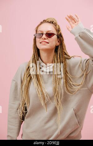 Freundliche Frau in Sonnenbrille mit stilvollen blonden afro Zöpfe über Rosa Hintergrund Stockfoto