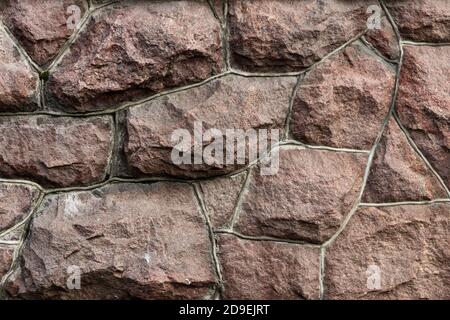 Die Oberfläche des Mauerwerks besteht aus grob behauenen großen roten Steinen, die miteinander verbunden sind. Stockfoto