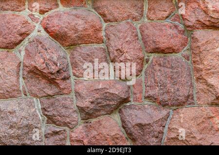 Die Oberfläche des Mauerwerks besteht aus grob behauenen großen roten Steinen, die miteinander verbunden sind. Stockfoto