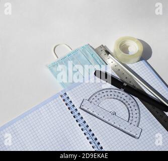 Notizbuch Winkelmesser Lineal Bleistifte Stifte Scotch-Band und medizinische Masken. Studie und Arbeit während einer Pandemie. Stockfoto