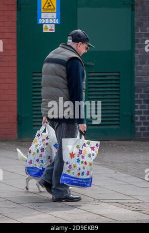 Ein älterer Mann, der Einkaufstaschen trägt, geht eine belebte Straße in der Innenstadt von Kennington London entlang. 28. April 2009. Foto: Neil Turner Stockfoto