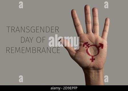 Nahaufnahme der Hand einer Person, in der ein Transgender-Symbol gemalt ist, und der Text Transgender Tag der Erinnerung auf grauem Hintergrund Stockfoto