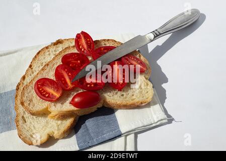 Ein Sandwich aus weißem hausgemachtem Brot und kleinen Tomatenscheiben. Ein scharfes Küchenmesser aus Stahl liegt in der Nähe. Gesunde Snacks. Vegetarismus. Stockfoto