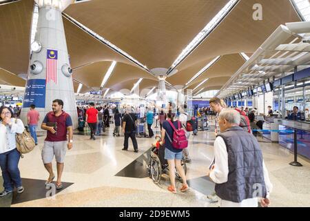 Reisende, die durch die Gegend gehen und ihre Abfertigungsschalter am identifizieren Hauptabflugshalle des Flughafens KLIA Stockfoto